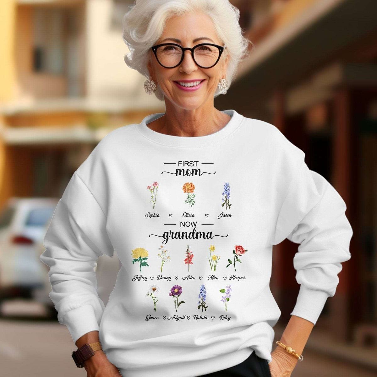 Model wearing a white First Mom Now Grandma sweatshirt with personalized birth flowers